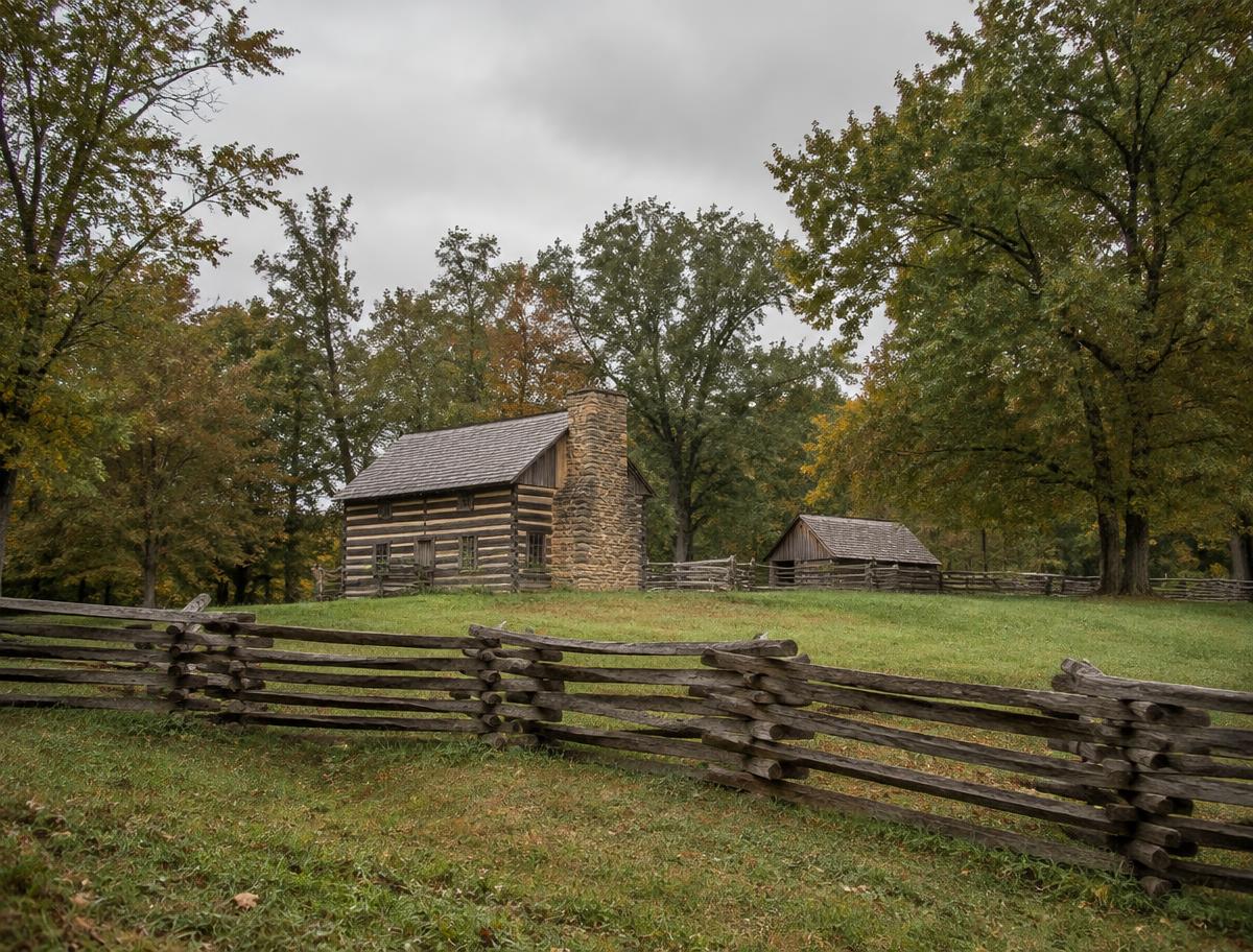 Illustration of period log buildings behind a split-rail fence